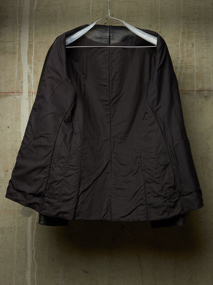 A dark brown quilted jacket hanging on a white hanger against a textured concrete wall.