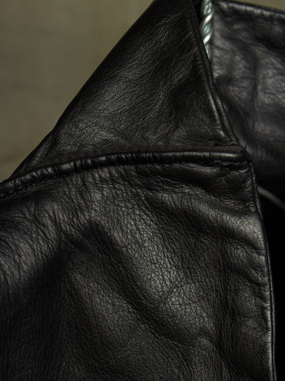 Close-up detail of a black leather jacket showing the texture of the leather, a stitched seam, and part of a silver zipper.