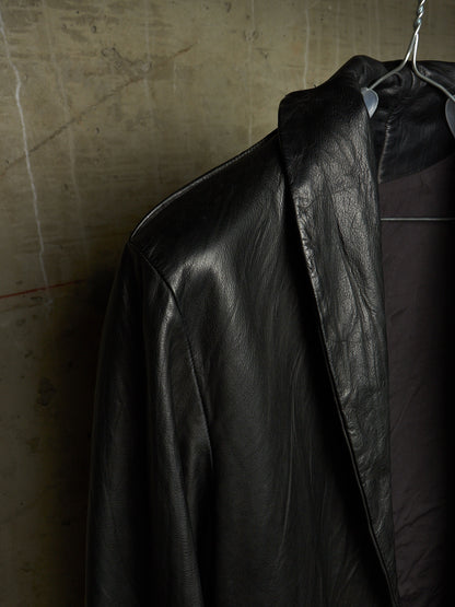 A black leather jacket hanging on a metal hanger against a textured concrete wall.