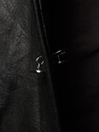 Close-up of a black leather jacket with a silver metal snap button closure, photographed in very dark lighting.