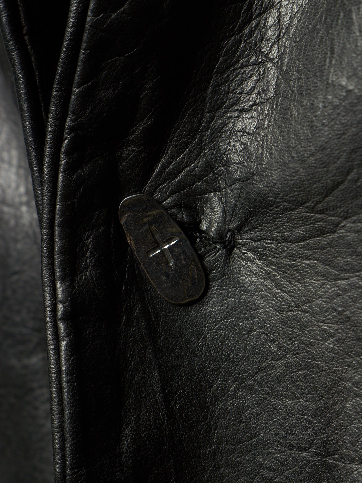 Close-up of a black leather jacket showing the textured grain and a dark button closure.