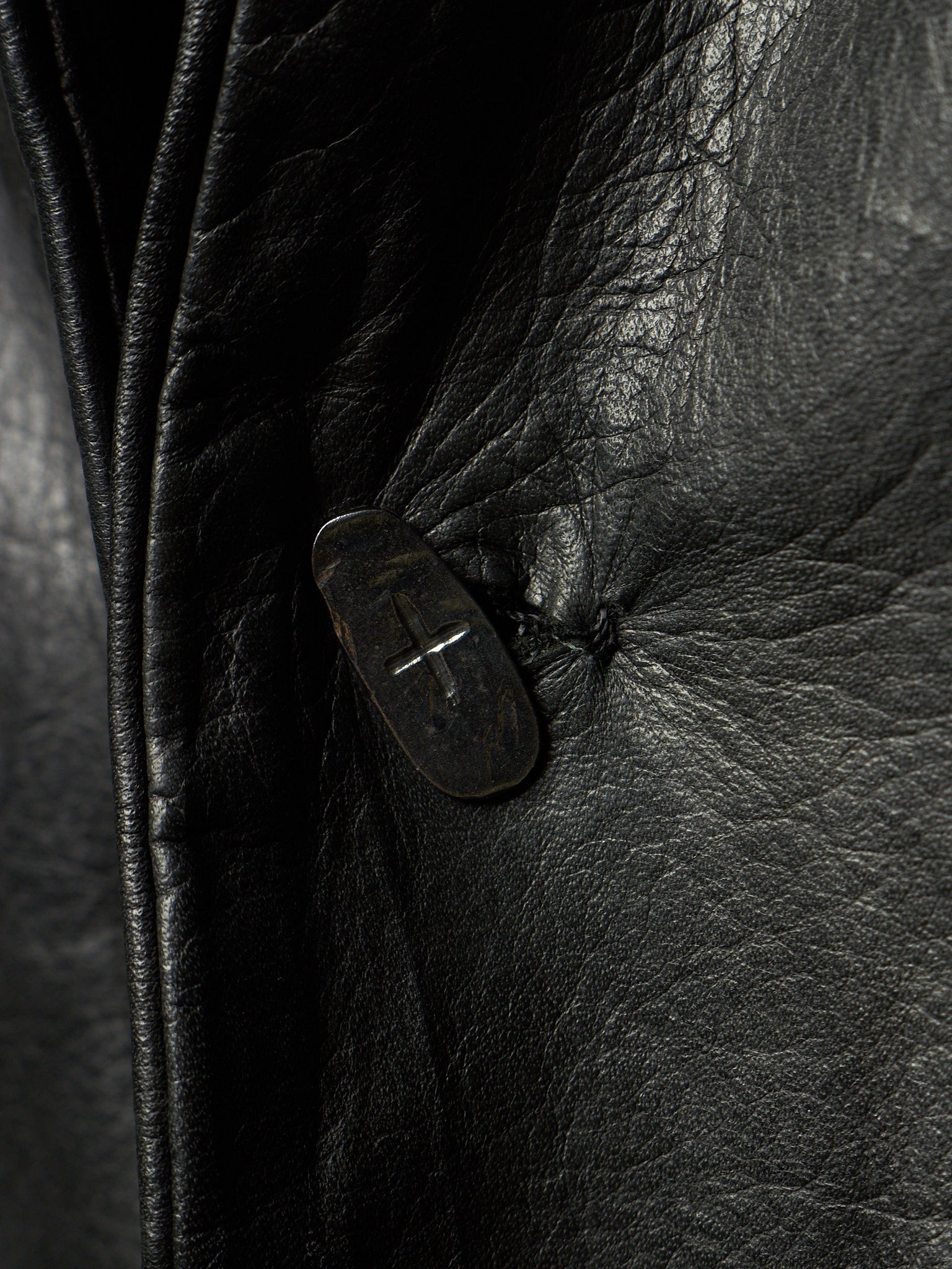 Close-up of a black leather jacket showing the textured grain and a dark button closure.