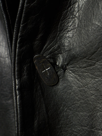 Close-up of a black leather jacket showing the textured grain and a dark button closure.