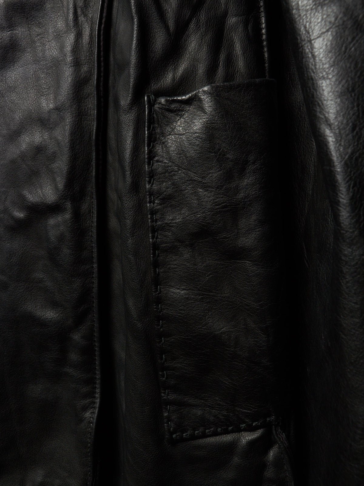 Close-up of a black leather jacket showing a stitched pocket and textured leather surface.
