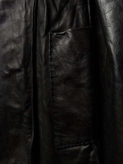 Close-up of a black leather jacket showing a stitched pocket and textured leather surface.