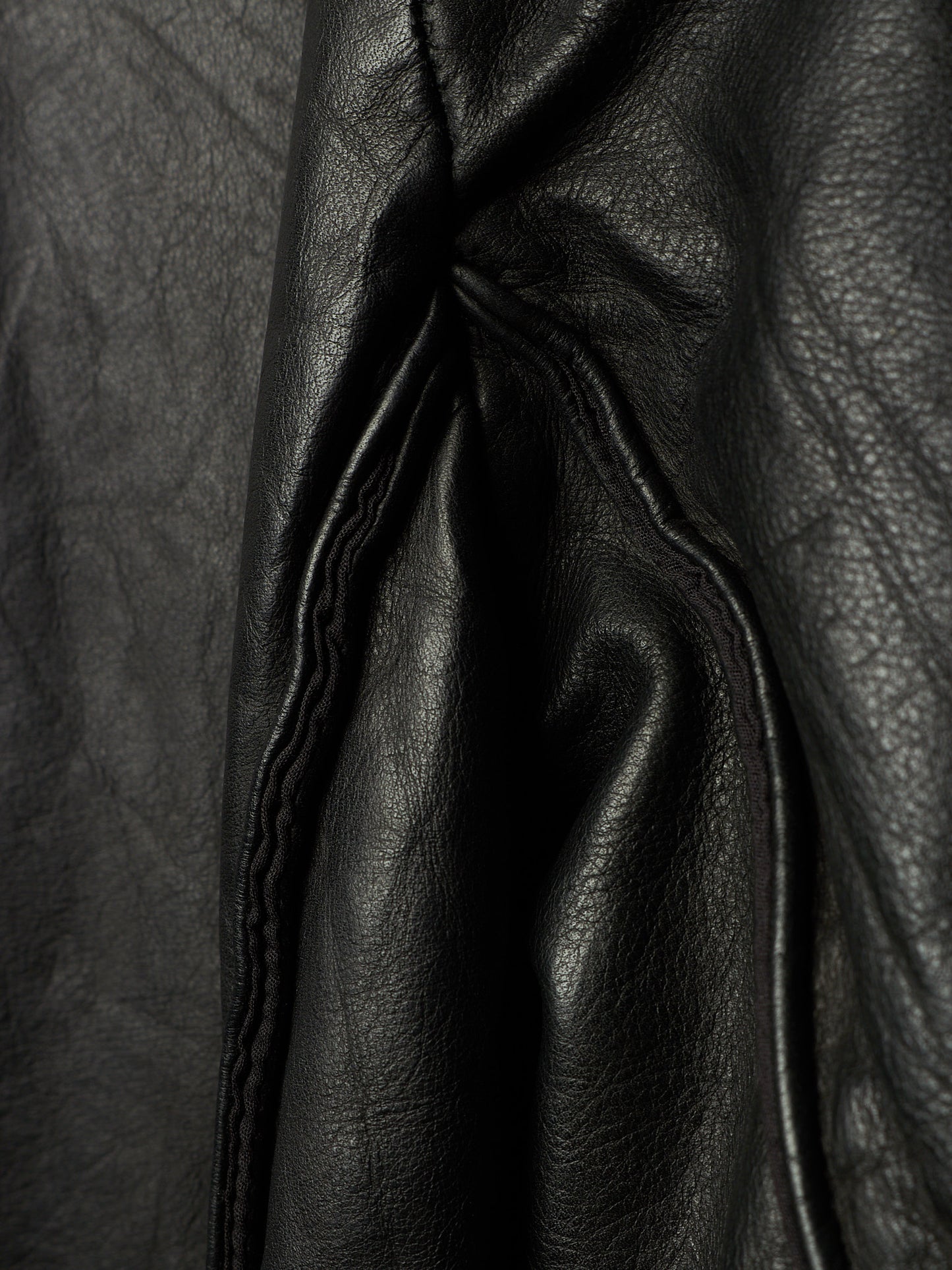 Close-up of black leather fabric with visible grain texture and stitched paneling.