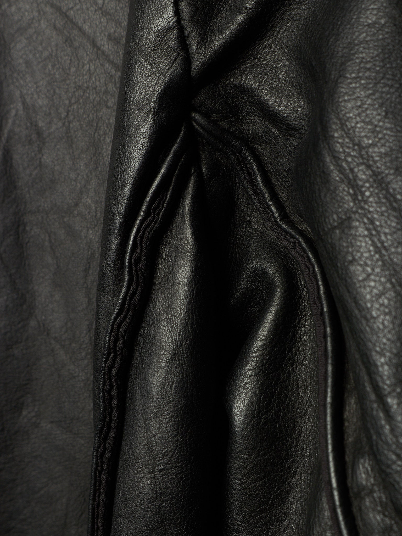 Close-up of black leather fabric with visible grain texture and stitched paneling.