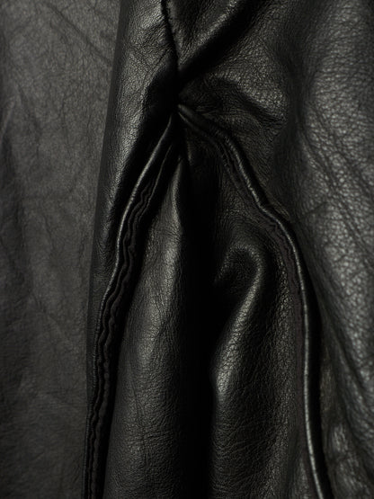 Close-up of black leather fabric with visible grain texture and stitched paneling.