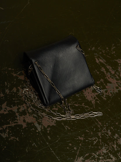 A black leather shoulder bag with a silver chain strap, photographed from an overhead angle on a dark, distressed textured surface.