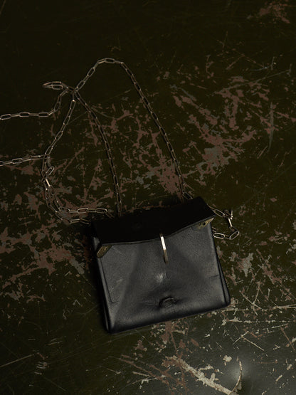 A black leather shoulder bag with a silver chain strap, photographed from above on a dark, distressed surface.