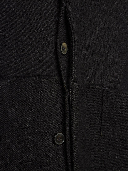 Close-up of a black textured fabric garment showing the button placket and pocket stitching.