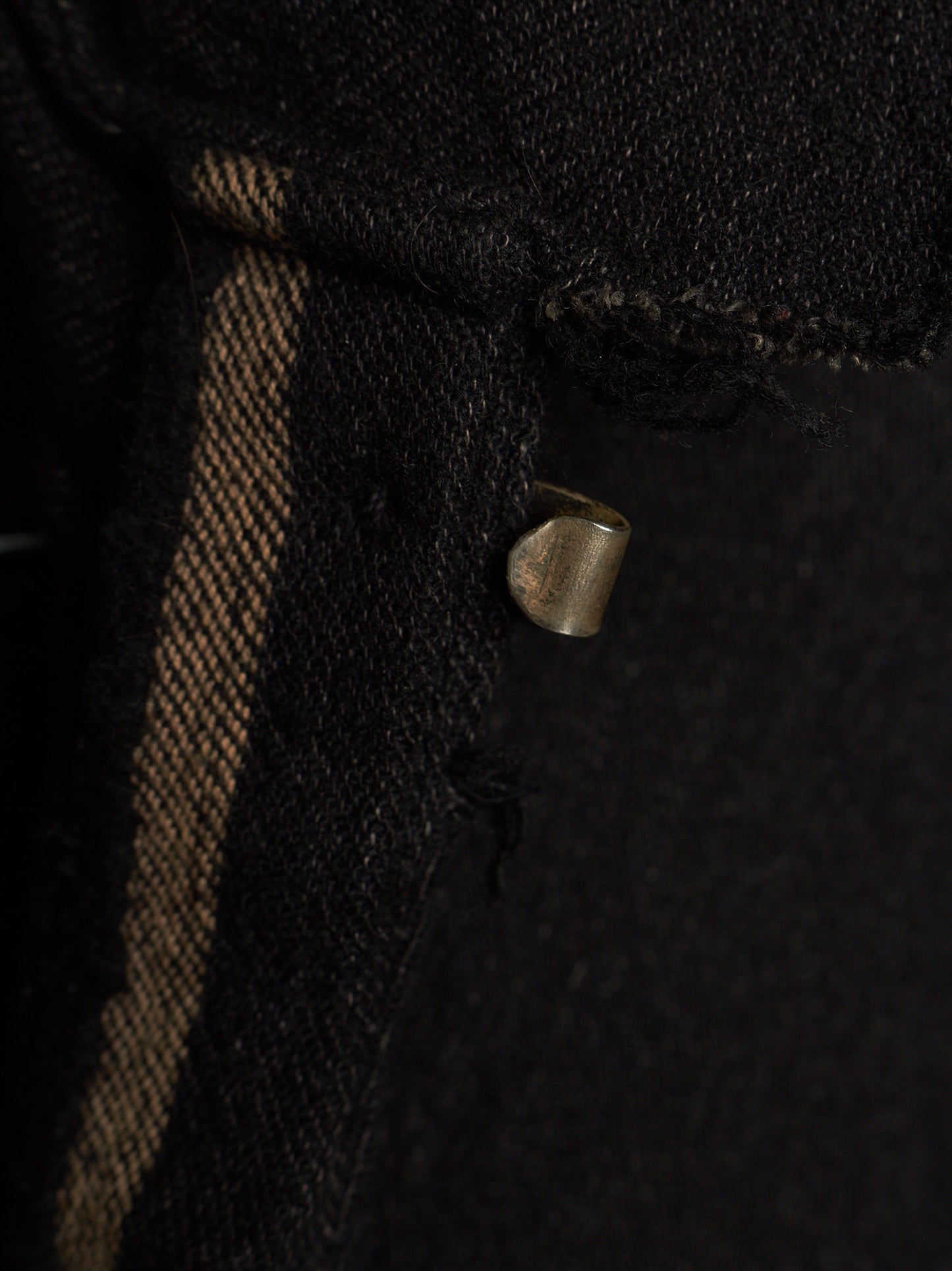 Close-up of a black woven textile with a vertical tan stripe and a small metallic loop detail.