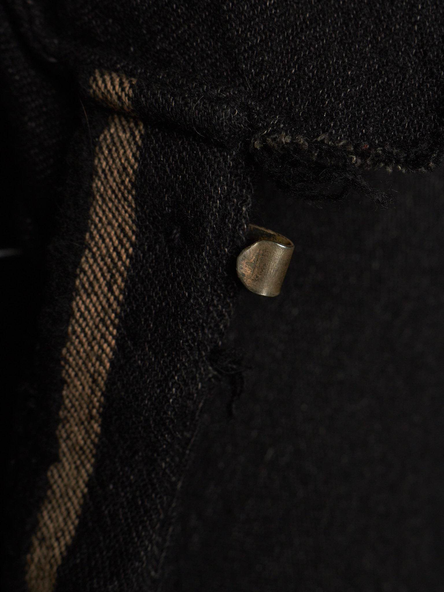 Close-up of a black woven textile with a vertical tan stripe and a small metallic loop detail.