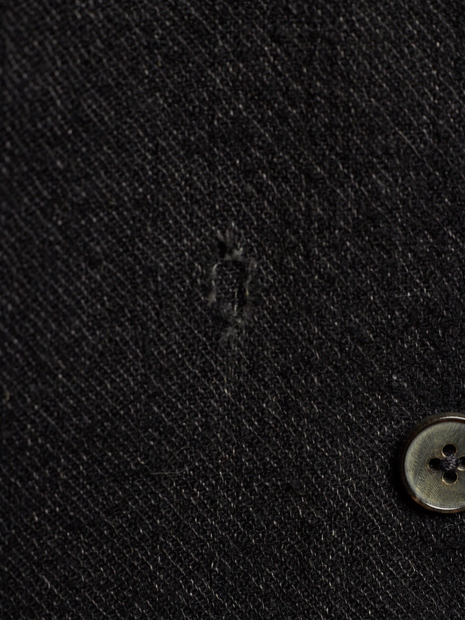 Close-up of a black textured fabric surface with a small button visible at the lower right.