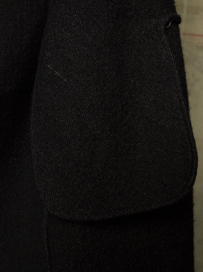 Close-up detail of a black textured fabric garment, showing a large patch pocket and the fine woven texture of the material.