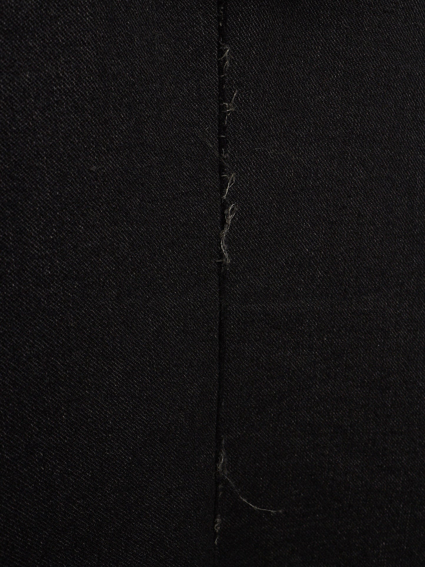 Close-up of black fabric with a central vertical seam and visible loose thread ends.