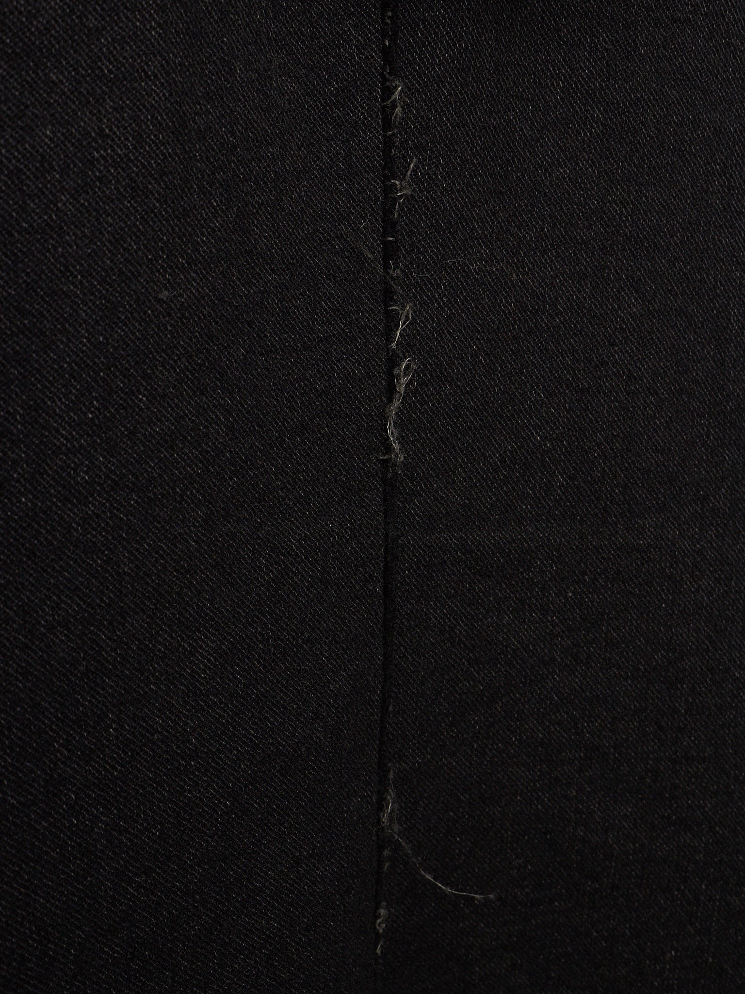 Close-up of black fabric with a central vertical seam and visible loose thread ends.