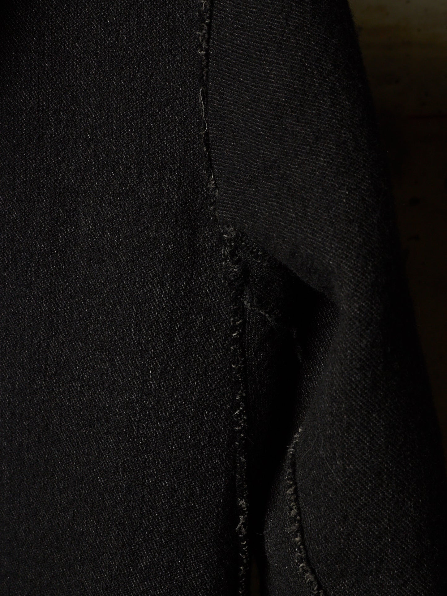 Close-up of a black textured fabric, likely denim, showing a raw, frayed seam detail.