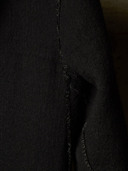 Close-up of a black textured fabric, likely denim, showing a raw, frayed seam detail.