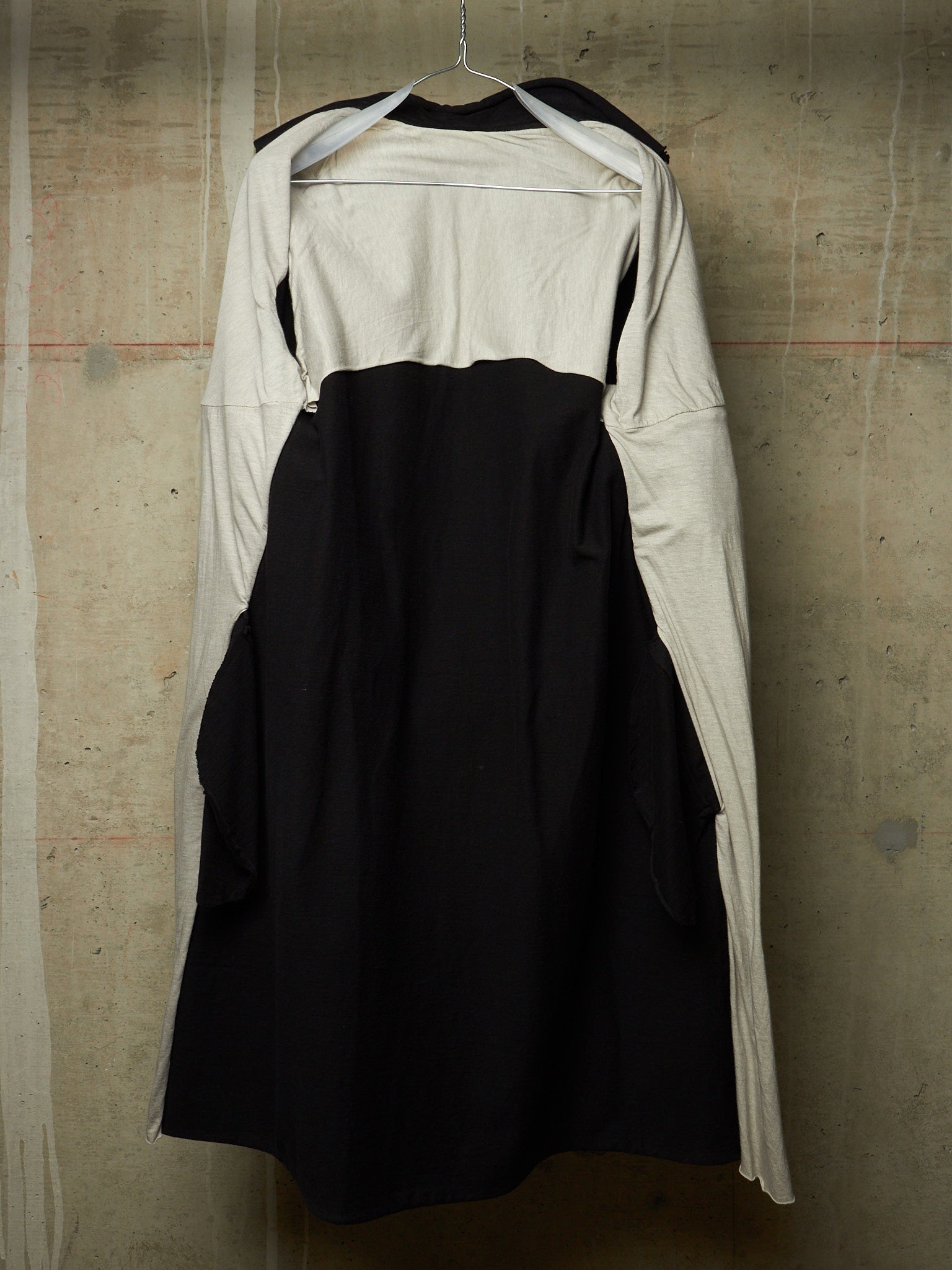 A black and off-white long-sleeve dress with a structured black bodice and flared skirt, hanging on a wire hanger against a textured concrete wall.