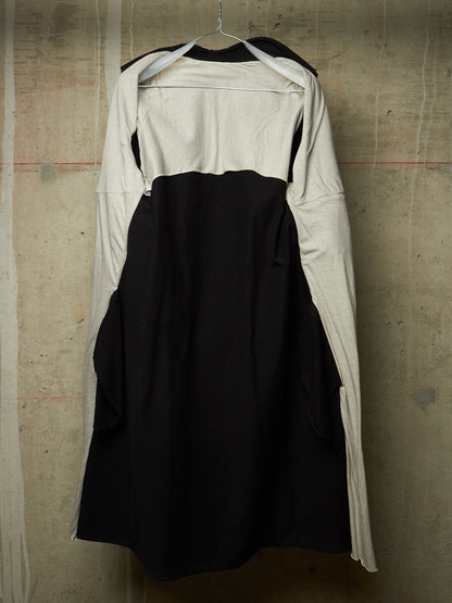 A black and off-white long-sleeve dress with a structured black bodice and flared skirt, hanging on a wire hanger against a textured concrete wall.