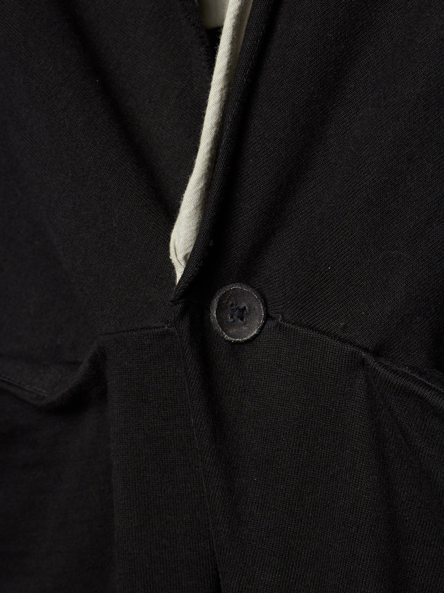 Close-up of a black textured fabric garment with a single dark button and a light off-white inner lining or trim visible at the neckline.