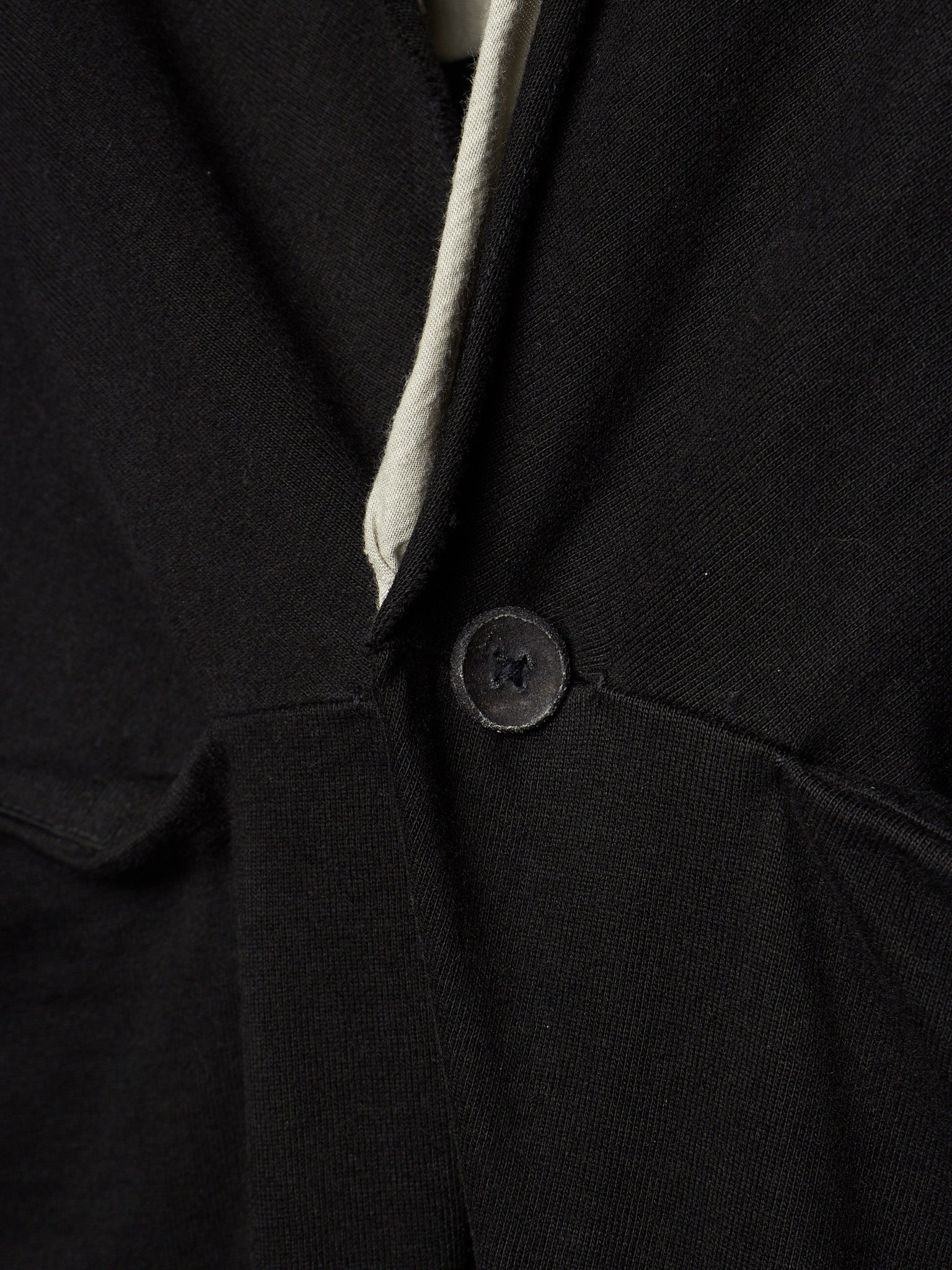 Close-up of a black textured fabric garment with a single dark button and a light off-white inner lining or trim visible at the neckline.