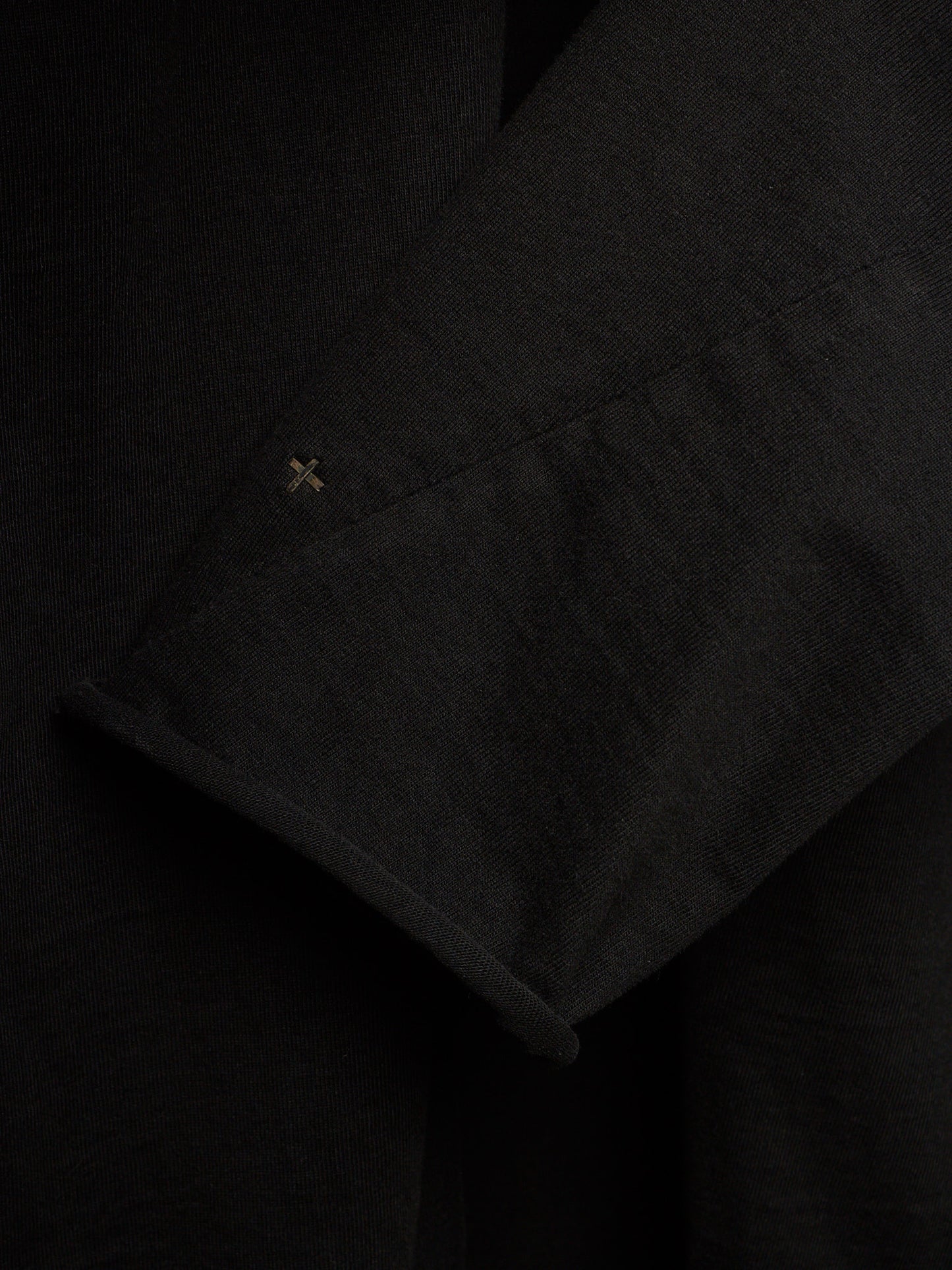 Close-up of a black textured fabric garment, showing a folded cuff with a small embroidered cross detail.