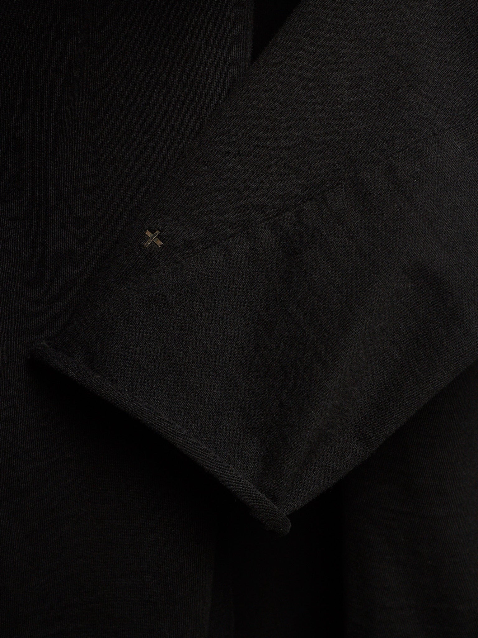 Close-up of a black textured fabric garment, showing a folded cuff with a small embroidered cross detail.