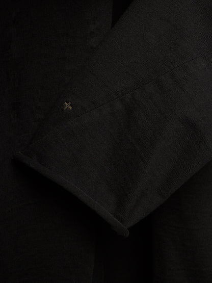 Close-up of a black textured fabric garment, showing a folded cuff with a small embroidered cross detail.