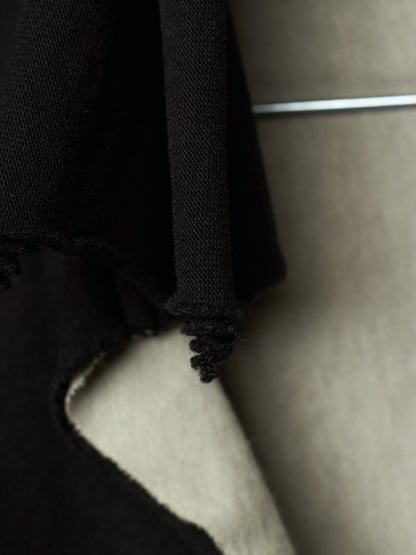 Close-up detail of a black knit garment with a frayed, cropped edge hanging against a neutral beige background.