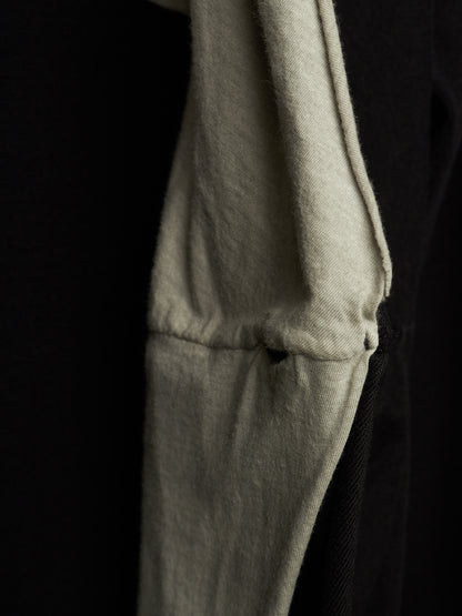 Close-up detail of a light beige or off-white fabric garment, showing a stitched seam and soft texture against a very dark black background.