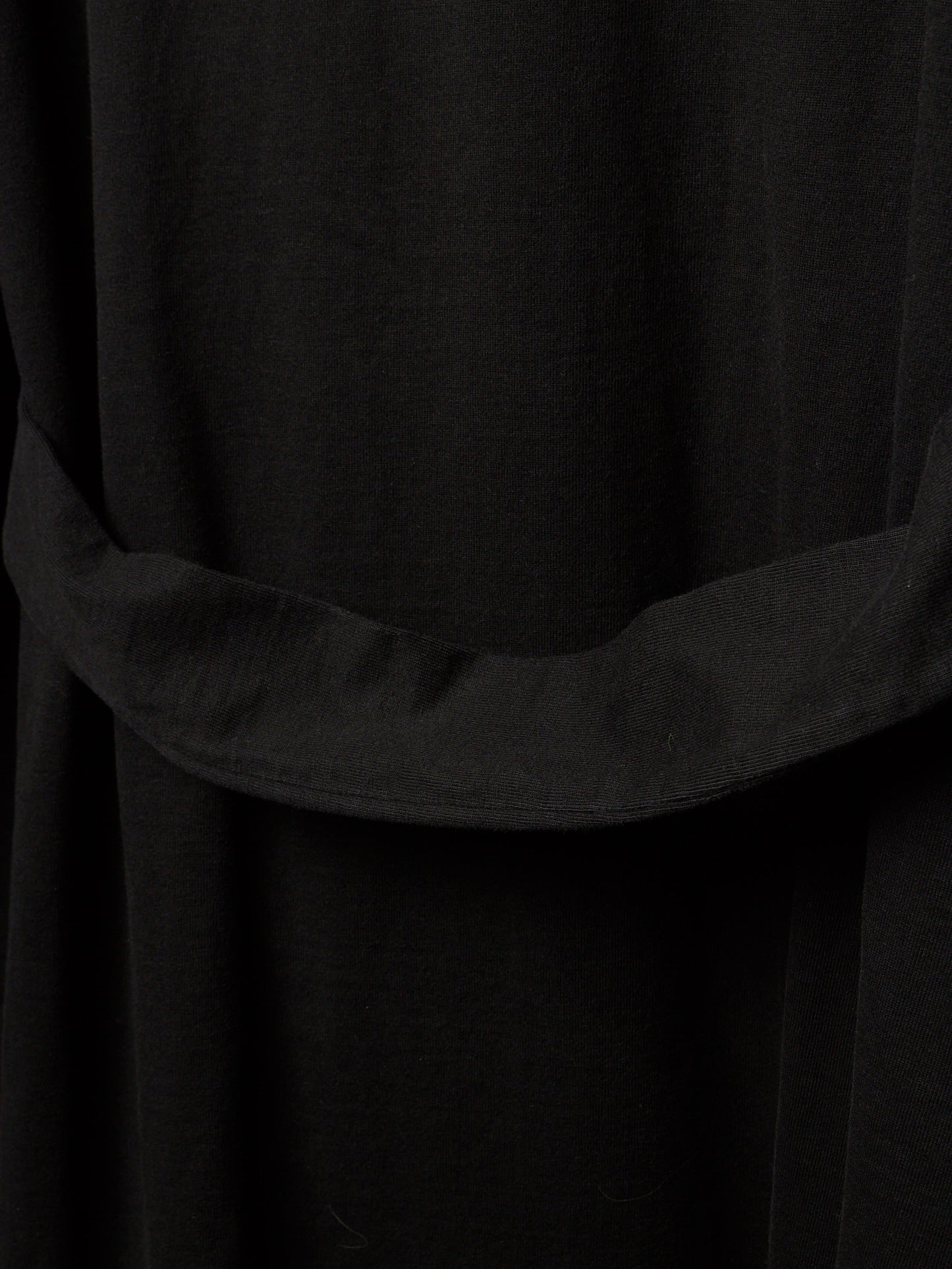 Close-up of a black fabric garment with a wide draped waist belt or sash detail.
