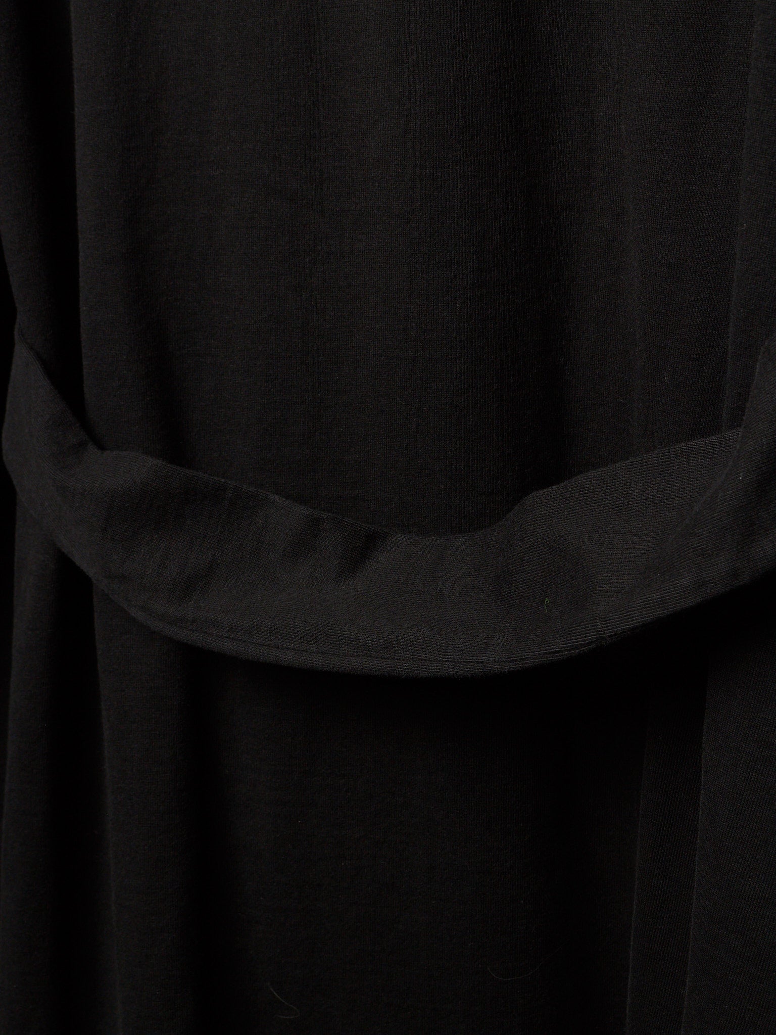 Close-up of a black fabric garment with a wide draped waist belt or sash detail.