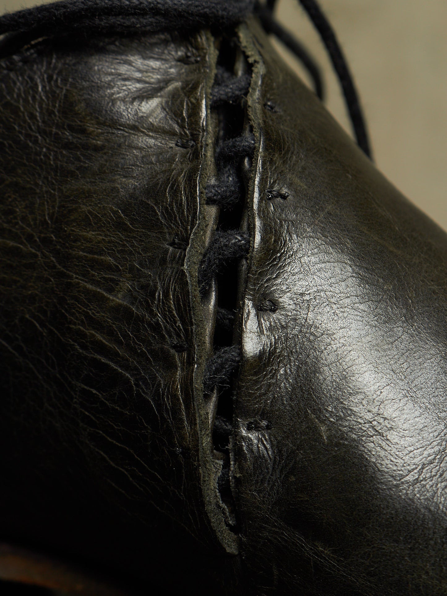 Close-up of a black leather boot with decorative hand-stitched laces running down the side.