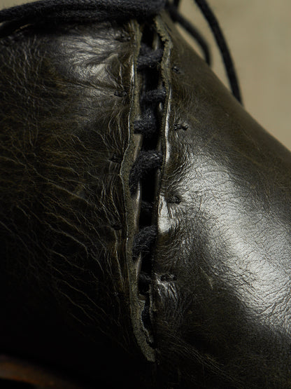 Close-up of a black leather boot with decorative hand-stitched laces running down the side.