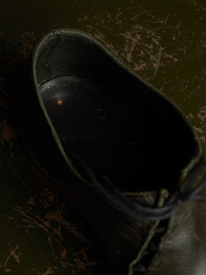 A close-up, high-angle view of the dark interior opening of a black lace-up shoe, set against a dark, distressed olive green background.