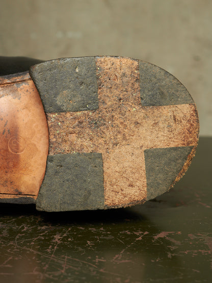 Close-up of the sole of a leather shoe, showing a cross-shaped patch of tan cork over dark gray rubber blocks, resting on a dark surface.