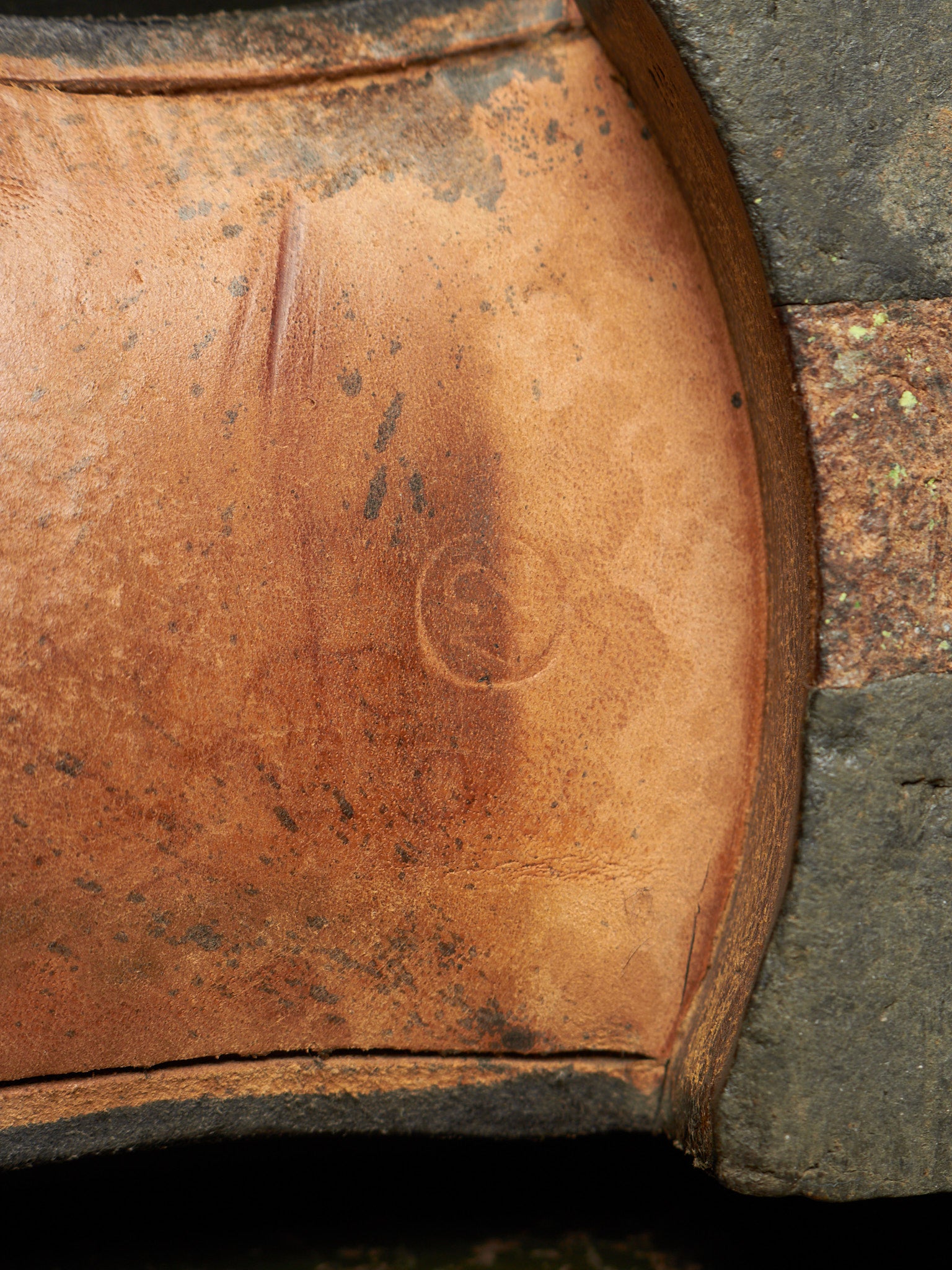 Close-up of a brown leather boot sole with a spiral embossed logo and a dark textured stone or rubber edge.