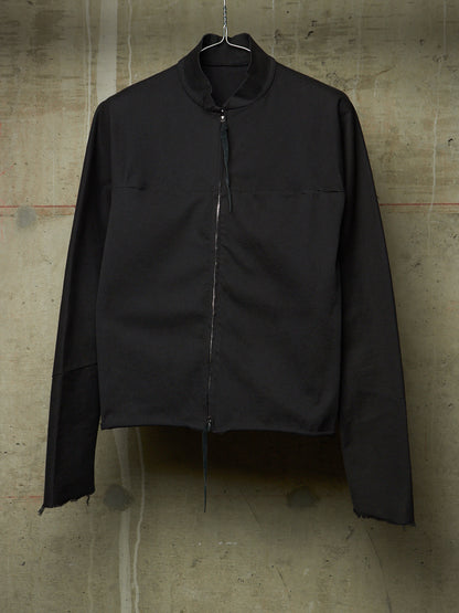 A black long-sleeve zip-up jacket with a high stand collar, hanging on a wire hanger against a textured concrete wall.