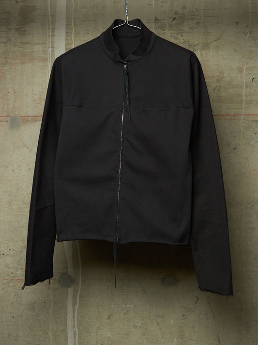 A black long-sleeve zip-up jacket with a high stand collar, hanging on a wire hanger against a textured concrete wall.