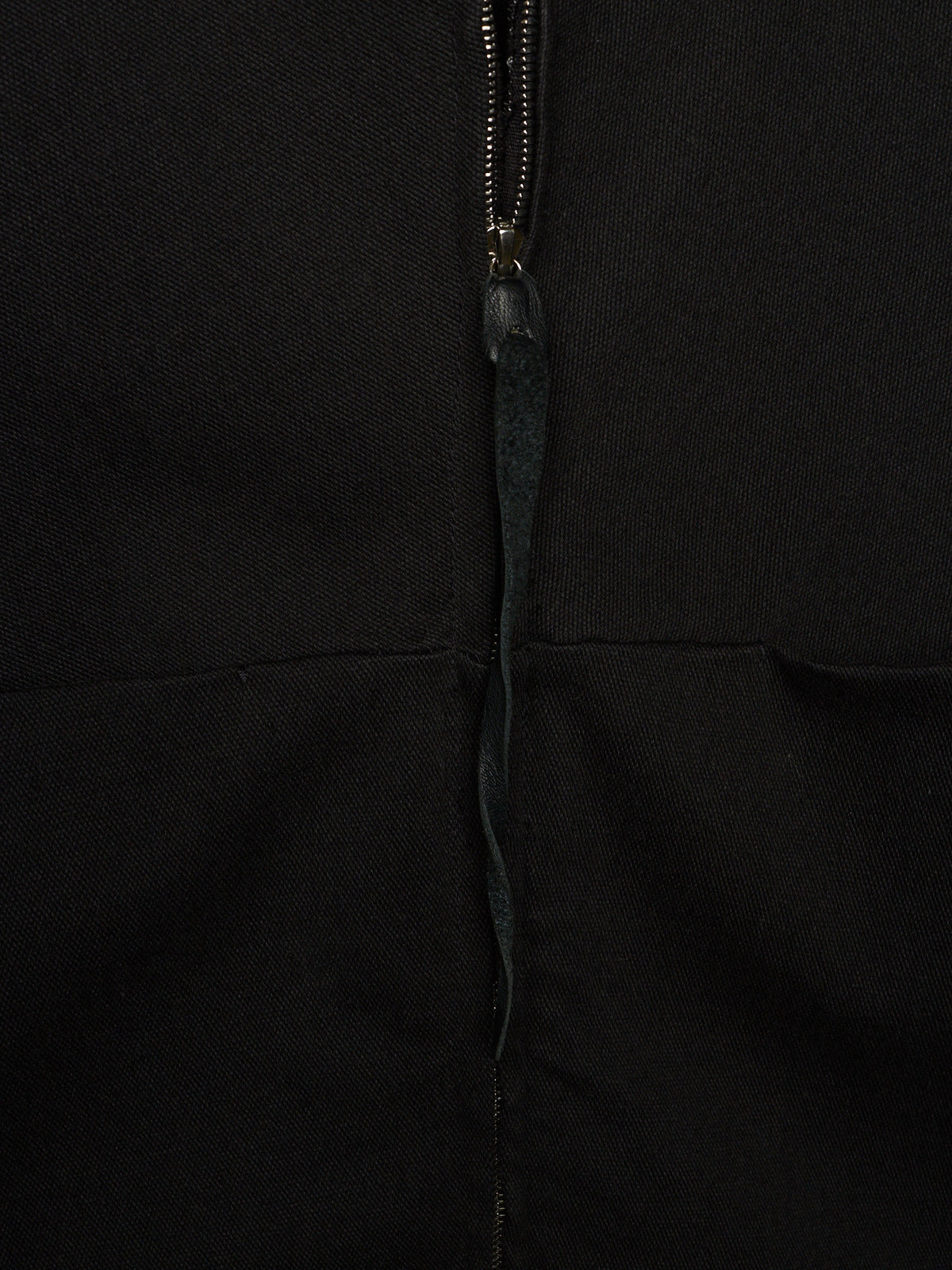 Close-up of a black garment featuring a central zipper with a dark pull tab.