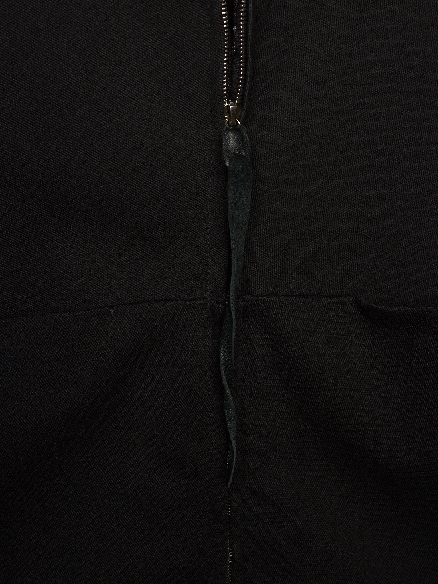 Close-up of a black garment featuring a central zipper with a dark pull tab.