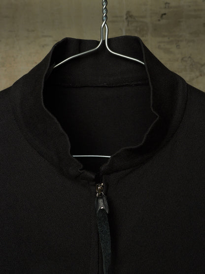 A close-up of a black knit zip-up sweater hanging on a metal hanger against a textured, warm-toned background.