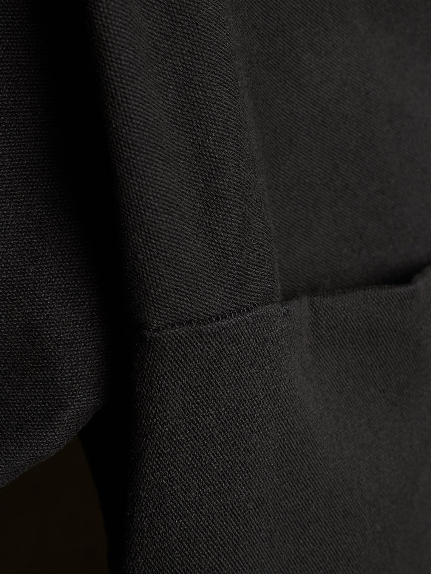 Close-up of a black textured fabric garment showing a seam and pocket detail.