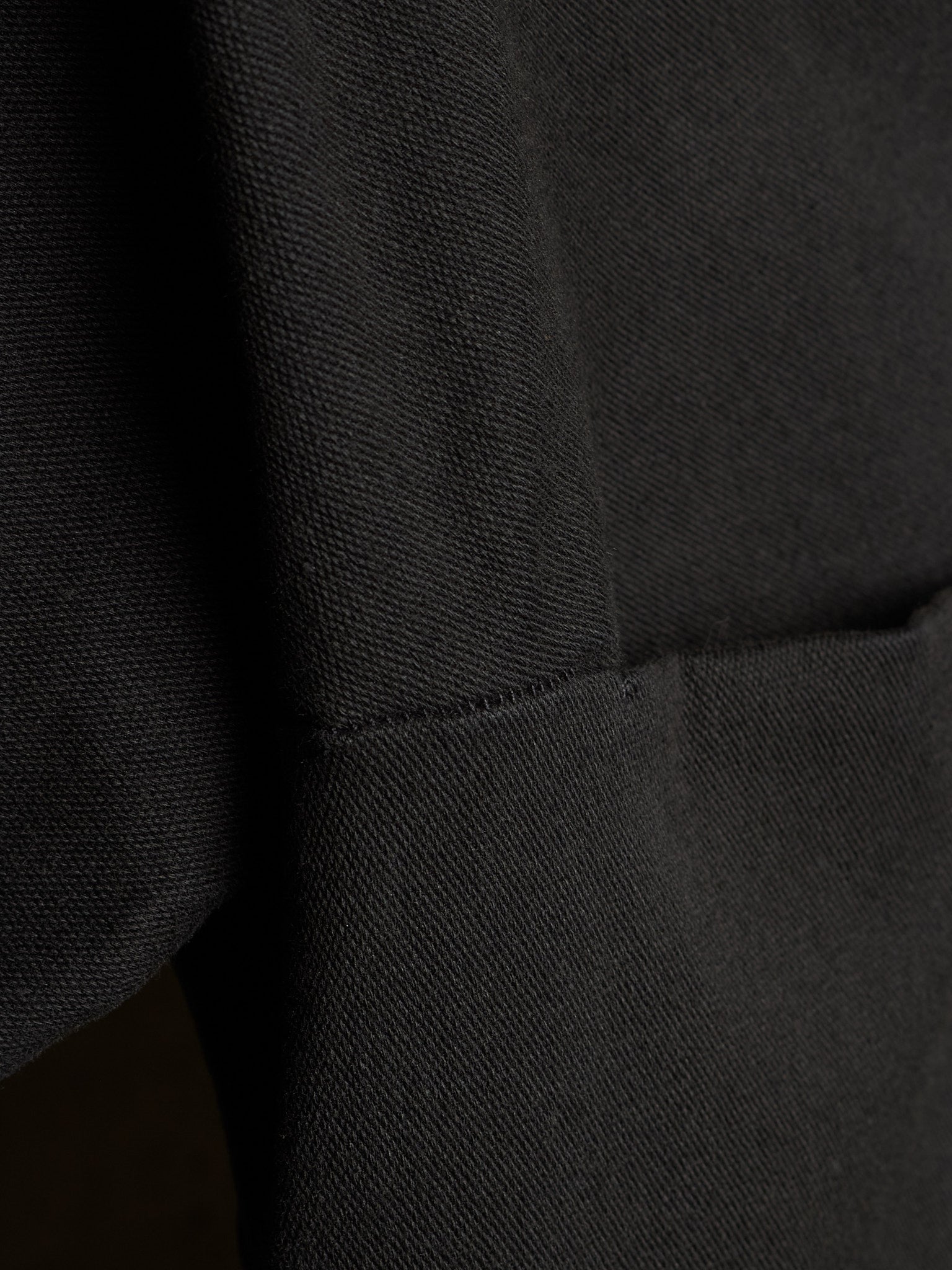 Close-up of a black textured fabric garment showing a seam and pocket detail.