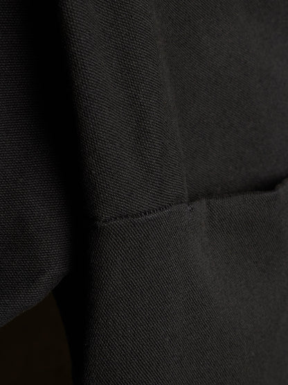 Close-up of a black textured fabric garment showing a seam and pocket detail.