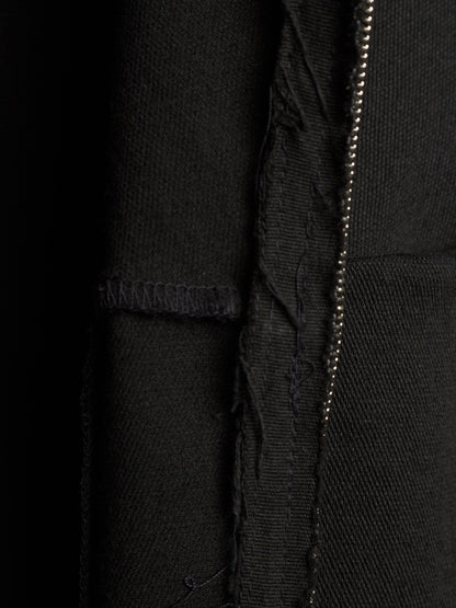 Close-up detail of a black textured fabric garment showing a vertical seam, raw frayed edge, and a metallic zipper running down the center.