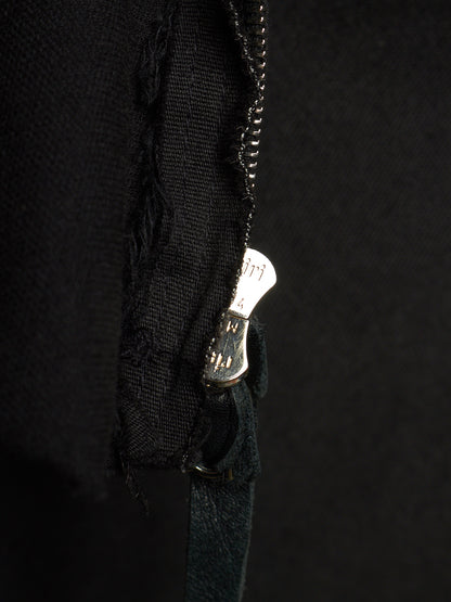 Close-up of a black fabric garment with a distressed, frayed edge and a silver metal zipper pull, set against a dark black background.