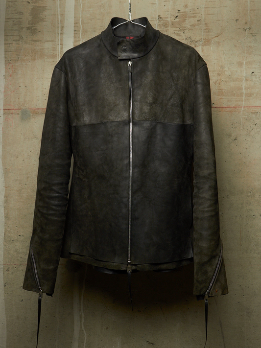 A dark brown leather jacket with a high mock neck collar and front zipper, hanging on a wire hanger against a textured concrete wall.